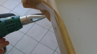 Isı tabancası olan bir adam mutfakta tadilat yapıyor. Isı tabancası yüzeyi ısıtır, bu da eski kaplamayı kolayca kaldırmaya yardımcı olur. İnşaat saç kurutma makinesi. Yüksek kalite 4k görüntü