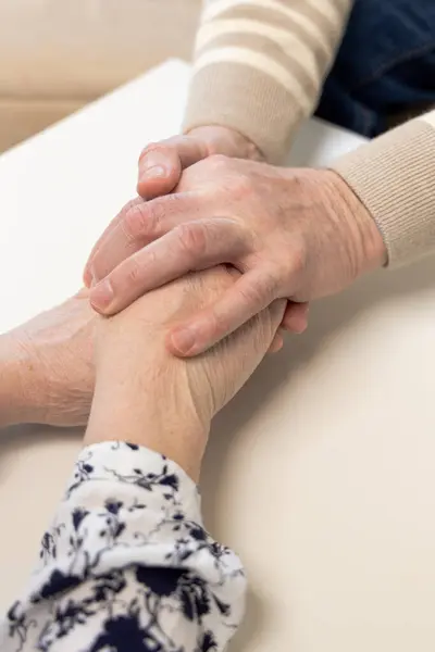 Yaşlı insanların elleri, şefkatli bir jestle birleşti, birlikte uzun bir hayat. Bir eldeki alyans sadakat ve sadakati işaret ediyor. Yıllarca birlikte yaşamış insanlar arasında derin bir bağ var.