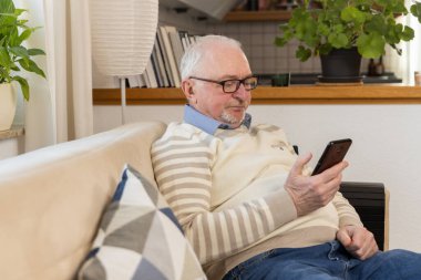 Evde dizüstü bilgisayarı olan yaşlı bir adam, uzaktan çalışma ve dijital iletişim eğilimi. Yaşlı insanlar teknolojiyle aktif olarak etkileşime geçip yeni beceriler geliştiriyorlar. Uzaktan çalışma ve dijital müdahale. Yüksek kalite