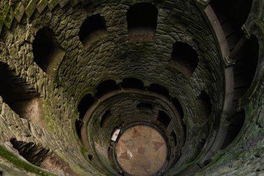 Sintra, Portekiz - 1 Mayıs 2024 - Ziyaretçiler, yosun kaplı kemerleri ve antik duvarları olan bir spiral taş olan Quinta da Regaleira 'nın Poco Iniciatico' sunu keşfediyorlar. Yüksek kalite fotoğraf