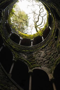 Sintra, Portekiz - 1 Mayıs 2024 - Ziyaretçiler, yosun kaplı kemerleri ve antik duvarları olan bir spiral taş olan Quinta da Regaleira 'nın Poco Iniciatico' sunu keşfediyorlar. Yüksek kalite fotoğraf