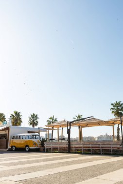 Malaga, İspanya, 02,04,2025 Suya bakan, palmiye ağaçlarıyla çevrili bir açık hava kafe kaygısız bir atmosfer yaratır. Bara dönüştürülmüş bir retro minibüs mekana cazibe ve benzersizlik katar. Yüksek