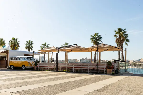 Malaga, İspanya, 02,04,2025 Suya bakan, palmiye ağaçlarıyla çevrili bir açık hava kafe kaygısız bir atmosfer yaratır. Bara dönüştürülmüş bir retro minibüs mekana cazibe ve benzersizlik katar. Yüksek