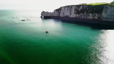 Güneşin altında kayalık sahillerde balıkçı teknesi. Fransa kıyılarında beyaz balıkçı teknesi Etreta 'nın yüksek uçurumlarına karşı. Yüksek kalite 4k görüntü