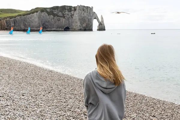 İlkbaharın başında Etretat 'ta kayalık plajda yürüyen günlük kıyafetli genç bir kız. Manş Denizi 'nin sakin suları. güneşli bir gün.