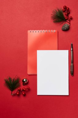 kırmızı zemin üzerinde boş bir not defteri, kalem ve noel süslemeleri ve kendi metin veya resminiz için boşluk