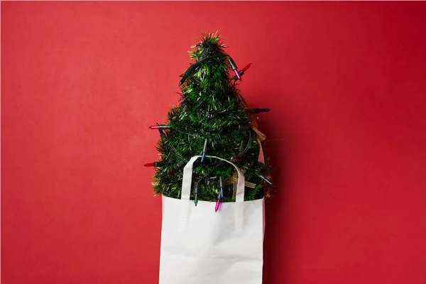 a christmas tree in a white paper bag on a red wall with scissors and other items hanging from the top