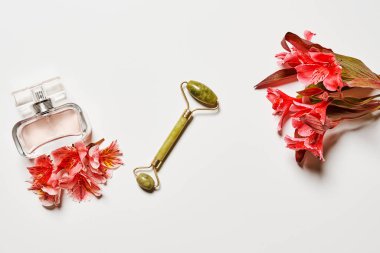 Beyaz bir yüzey üzerinde çiçekler ve parfüm şişeleri. Altyazılar için boşluk var.