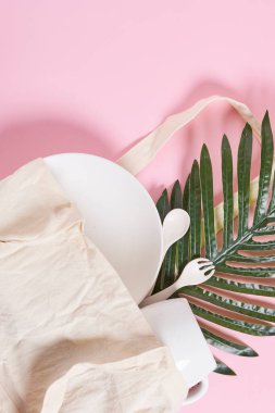 Beyaz bir tabak ve pembe arka planda yeşil yapraklar var. Resimde boş bir kese kağıdı var. Yukarıdan alınmış.