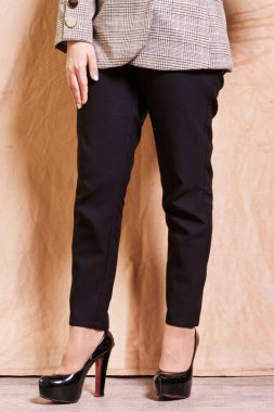 Duvarın önünde duran bir kadın takım elbiseli ve yüksek topuklu ayakkabılı elleri kalçasında.