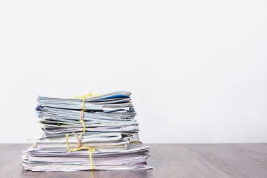 Beyaz bir duvarın önündeki ahşap bir masanın üzerinde, kenarları sarı şeritli bir gazete yığını.