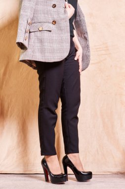 Duvarın önünde duran siyah beyaz kareli ceketli, düğmeli bir kadın.