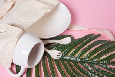 Fincanda palmiye yaprakları olan pembe arka planda iki beyaz bardak kahve fincanı ve kaşığın yanında.