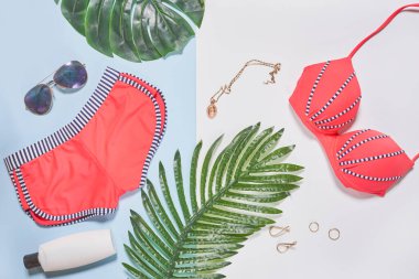 Bikiniler, güneş gözlükleri ve açık mavi arka planda palmiye yaprakları. Yazın burada olduğunu söyleyen metin.