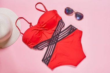 Kırmızı mayo ve pembe arka planda güneş gözlüğü, hasır şapka, güneş ve plaj havlusu.