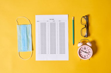 Koronavirüs için göz çizelgesi olan sarı arka planda bir saat, gözlük ve maske.