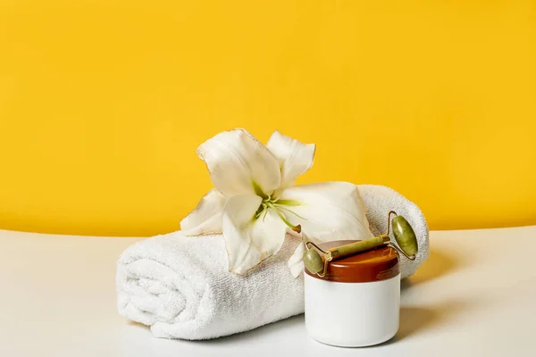 a white towel with a flower on it and a cup of hot tea sitting next to it in front of a yellow wall
