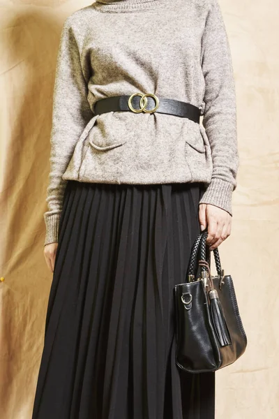 一个女人 手里拿着一个黑色的手提包 穿着一件灰色的毛衣 脖子上戴着一个金戒指 站在一个 — 图库照片