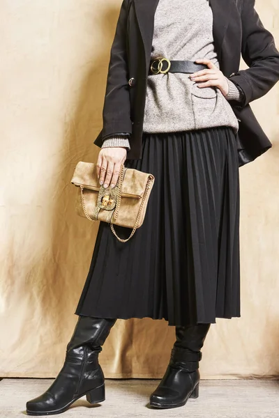 黒いコートを着て右手に茶色の財布を持ちながらベージュの壁に立っている女性は — ストック写真