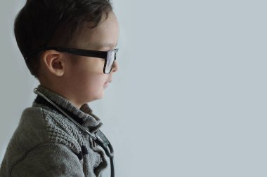 Küçük bir çocuk gözlük takıyor ve eli cebinde duvardaki bir şeye bakıyor.