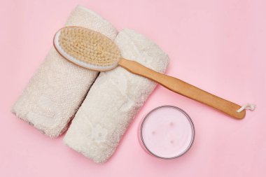 a wooden brush and towel next to a bowl of tooth paste on a pink background with copy space for text