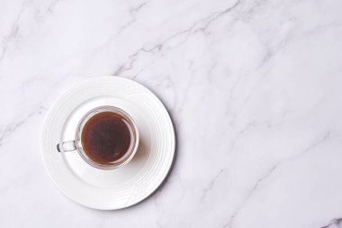 a cup of coffee on a white plate with a spoon in the middle, and a marble surface behind it
