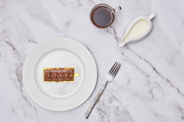 a piece of cake on a plate next to a cup of coffee and a spoon with chocolate frosting in it
