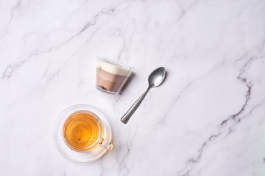a cup of tea and a spoon on a marble table with white marble countertops in the photo is taken from above
