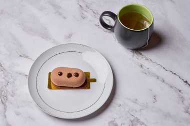 a sandwich on a plate with a cup of tea in the background and a coffee mug sitting next to it