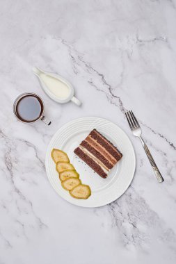 a piece of cake on a plate with a fork and knife next to it, sitting on a marble table