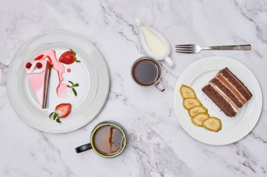 some desserts and coffee on a marble table with two plates full of cake, one slice is topped with strawberries