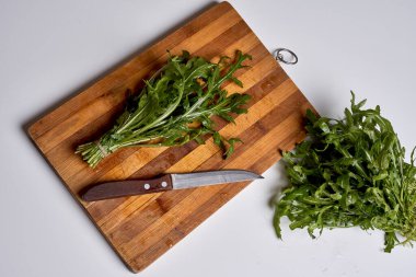 some greens on a cutting board next to a knife and a piece of lete with its end cut in half