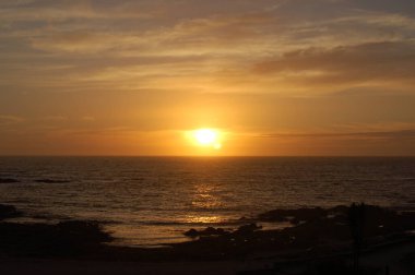 Cantabrian Denizi 'ndeki güzel günbatımı manzarası ve üzerinde turuncu gökyüzü. Arka plan olarak sakin dalgalara çarpıcı bir altın güneş yansıması. Sahilde yaz günbatımının muhteşem manzarası. Doğa