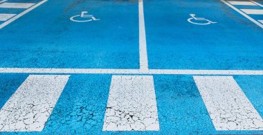 Mavi asfalt üzerinde engelliler için ayrılmış çift boş park yeri. Uluslararası engelli sembolü beyaza boyanmış, mekanın parlak mavisiyle. Mekan ikisinde de açıkça işaretli.