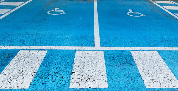Двойное бесплатное парковочное место, зарезервированное для рук на синем асфальте с международным символом handdicap, выкрашенным в белый цвет с ярко-синим цветом пространства. Пространство четко отмечено на обоих