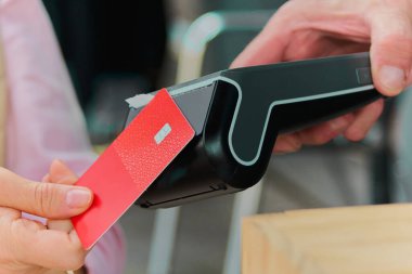 Yetişkin kartıyla ödeme yapan bir kadın, bir erkeğin elinde bulunan kablosuz elektronik kart ödeme terminalinde çalışıyor..