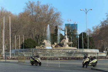 Madrid's Fountain of Neptune, guarded by police motorcycles and barriers, combines classical beauty with modernity and city security.