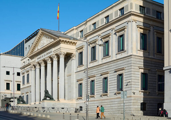 The iconic neoclassical facade of the Congress of Deputies, with its majestic columns and a golden lion statue guarding the main entrance, symbolizes Spanish political power