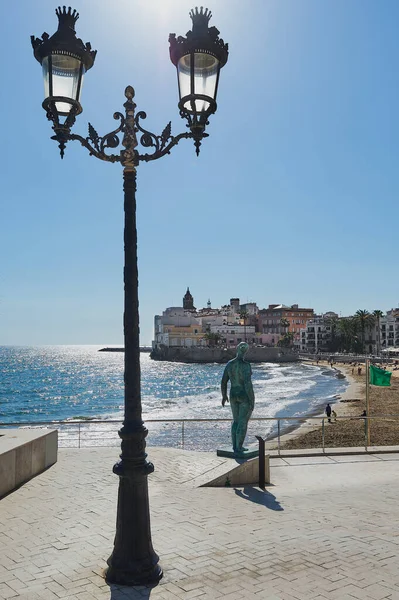 stock image Classical statue of a naked woman looking towards the city of Sitges with people on the beach and the green flag of bathing allowed and a bicycle in the foreground on a sunny day in Catalonia, Barcelona, Spain