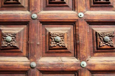 Merkezinde yuvarlak metal parçaları olan eski bir kapının ahşabındaki çiçek desenini oymak. Eski bir kapının ahşabında, merkezde yuvarlak ve yuvarlak detaylar bulunan bir çiçek tasarımı.