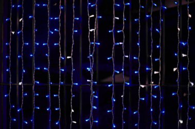 Beyaz dikey perdelerle süslenmiş Noel çelenkleri ve siyah arka planda izole edilmiş beyaz ve mavi yuvarlak ışıklar..