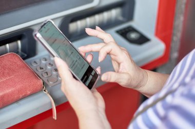 Banka ATM 'sinin önünde elinde cep telefonu olan tanınmayan bir kadın online bankacılık operasyonu yürütüyor..