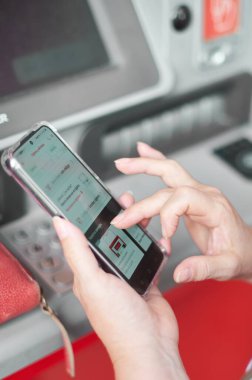 Banka ATM 'sinin önünde elinde cep telefonu olan tanınmayan bir kadın online bankacılık operasyonu yürütüyor..