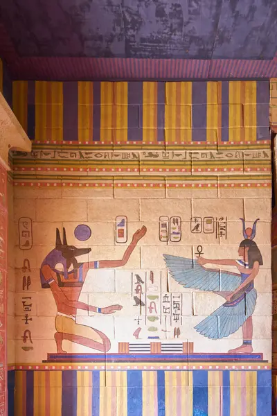 Ancient Egyptian mural depicting two figures, one with the head of a jackal representing the god Anubis and the other with the head of a cow representing the goddess Hathor. The figures are in profile