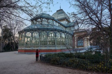 Gün batımında Madrids Retiro Park 'taki Viktorya dönemi cam sarayında kırmızı ceketli bir kadın fotoğrafını çekiyor..