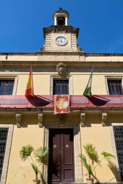 Jerez de la Frontera Belediye Binası 'nın açık mavi gökyüzünün altındaki saat kulesi ve bayraklarıyla manzarası.