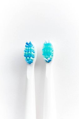 Mavi tüylü iki beyaz diş fırçasına yakın plan, biri yeni, diğeri beyaz arka planda kullanılmış..