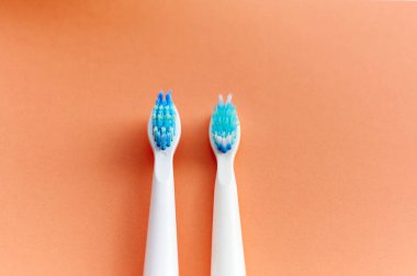 Mavi tüylü iki beyaz diş fırçasının yakın çekimi. Biri yeni diğeri ise turuncu arka planda kullanılmış..