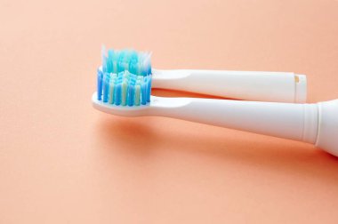 Mavi tüylü iki beyaz diş fırçasının yakın çekimi. Biri yeni diğeri ise turuncu arka planda kullanılmış..