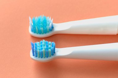 Mavi tüylü iki beyaz diş fırçasının yakın çekimi. Biri yeni diğeri ise turuncu arka planda kullanılmış..